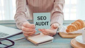 the woman holds in her hands a paper with the words “SEO audit”.